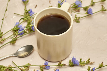 chicory drink in a coffee mug and a spoon next to chicory flowers