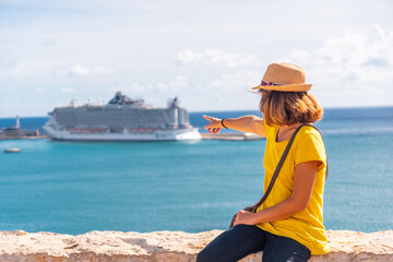 Fototapeta na wymiar A young woman pointing at the cruise ship that has arrived on the island of Ibiza from the castle wall, Balearic Islands, Eivissa