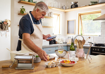 Senior man, cooking and phone for recipes, research or ingredients for the perfect meal in the kitchen at home. Elderly male cook or baker with food browsing online recipe or streaming on smartphone