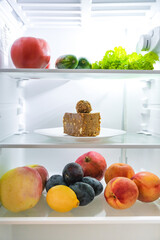 Refrigerator with sweets and fruits and vegetables.Piece of cake and healthy food.Diet carbohydrates.Junk food.Calories and benefits.Hand reaching for the cake