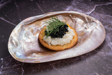 Black caviar served on an elegant shell with scrambled eggs and lemon on crackers.