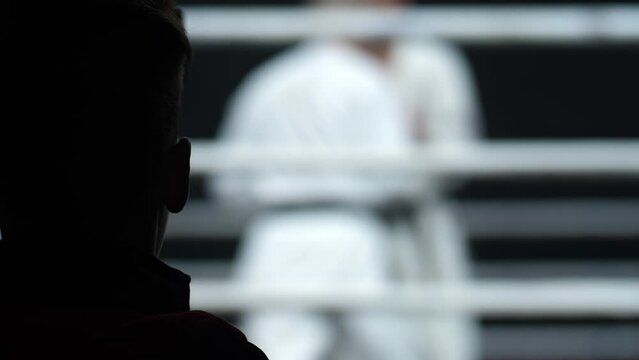 Silhouette of a man's head opposite the ring. A man watches a sports duel of karate.