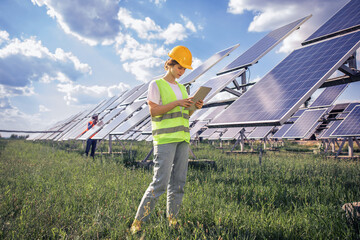 At photovoltaic solar farm charismatic woman ecological engineer walking and analysing the efficient of photovoltaic solar panels and analysing the operation of sun and cleanliness of photovoltaic