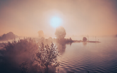Idylliczny, mglisty poranek nad wodą. Słońce przebija się przez mgłę, spokojna rzeka, cisza i...