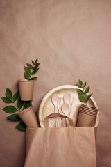 Eco-friendly packaging and tableware set on brown paper background with green leaves and copy space.