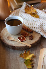 Fototapeta premium Cup of tea or coffee, seasonal spices, bowl of cookies, blanket, pumpkins, colorful leaves, books and tangerines on wooden table. Cozy hygge at home. Selective focus.