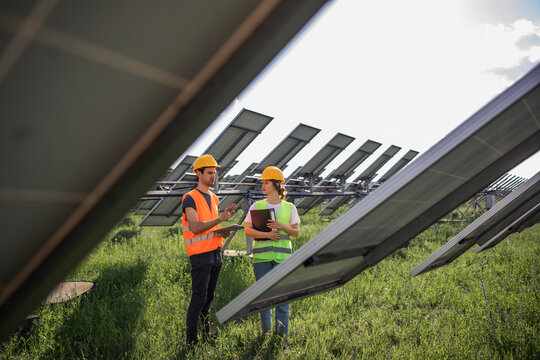 Portrait of electrician engineers in safety helmet and uniform checking solar panels. Group of two engineers at solar station.