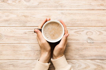 Minimalistic style woman hand holding a cup of coffee on Colored background. Flat lay, top view cappuccino cup. Empty place for text, copy space. Coffee addiction. Top view, flat lay