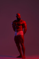 Fototapeta na wymiar Athletic man demonstrates muscles in the light of a red light filter on a dark background.