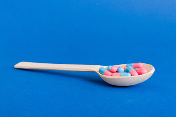 Vitamin capsules in a spoon on a colored background. Pills served as a healthy meal. Red soft gel...