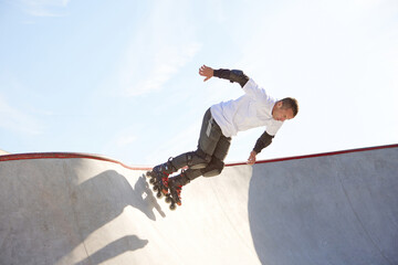 Mature male inline roller training in public skate park. Practicing jumps, tricks. Concept of...