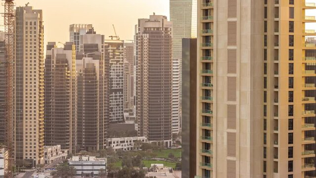 Skyscrapers at the Business Bay in Dubai aerial timelapse during all day with shadows mobing fast. Green lawn with palms in the yard, United Arab Emirates