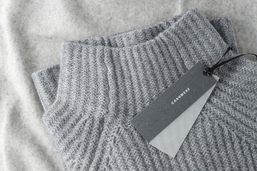 Soft textured sweater of grey luxury natural cashmere with blank paper tag lying on light wool...