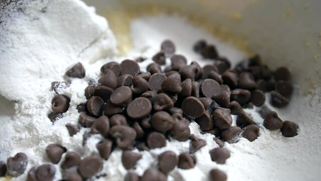 Close up of chocolate chips being added to cookie dough cake mix with flour butter and sugar