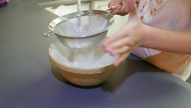 A girl sieving flour into a bowl for baking