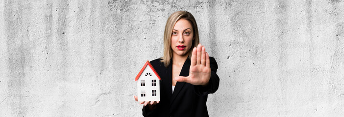pretty blonde woman looking serious showing open palm making stop gesture. real state concept