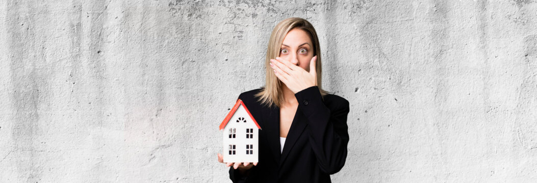 pretty blonde woman covering mouth with hands with a shocked. real state concept