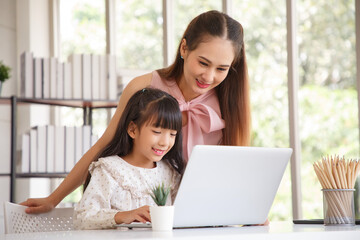 Children education and home school concept : Young asian mother pleased to see little daughters' study online. Excited smiling child girl enjoying online learning  with pleasant mom at home.