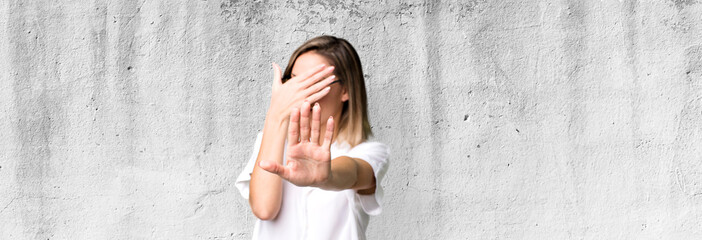 blonde adult woman covering face with hand and putting other hand up front to stop camera, refusing...