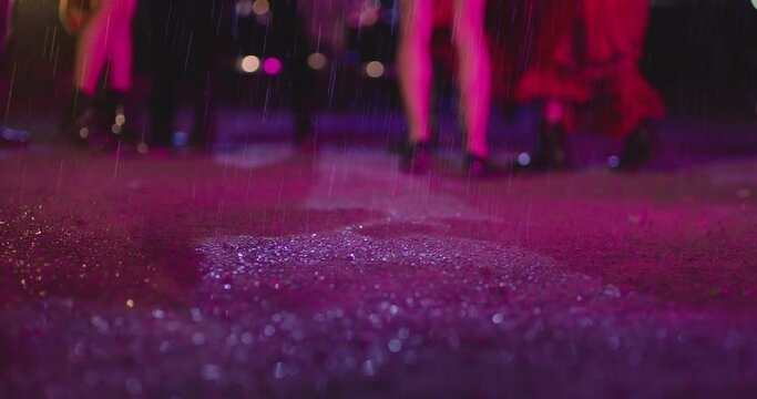 Footage of young people's feet and legs jumping and dancing in the rain at night . 150 fps Slow motion shot of different legs dancing on ground with puddle . Water splash at rainy day .
