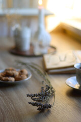 Cup of tea, plate with chocolate chip cookies, open book, reading glasses, lit candles and dry lavender flowers. Hygge at home, selective focus.