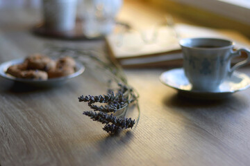 Cup of tea, plate with chocolate chip cookies, open book, reading glasses, lit candles and dry lavender flowers. Hygge at home, selective focus.