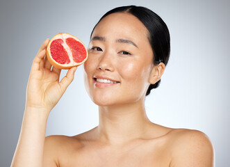 Grapefruit, skincare and woman with food for face, wellness and beauty against a grey mockup studio background. Portrait of young, happy and Asian model with fruit for nutrition, diet and body health