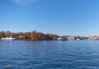 Obraz premium Panorama view, commuting steam boats and harbor ferries in the bay Ladugårdsviken with offices, apartment and hotel buildings a colorful autumn day in Stockholm