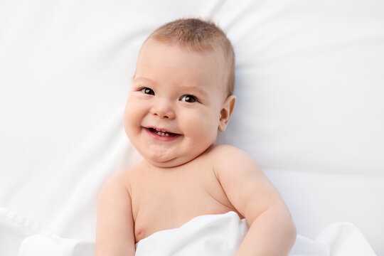 Happy baby lying on white bed looking at camera
