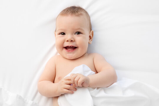 Smiling baby lying on white bed with mouth open