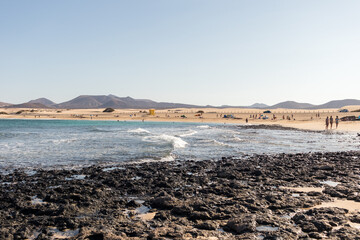 Amazing seascape of yellow sand beach and volcanic rocks with mountains in the distance.Fuerteventura, Canary Islands, Spain