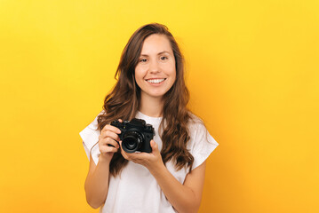 Close up portrait of young woman holding vintage photo camera over yellow background.