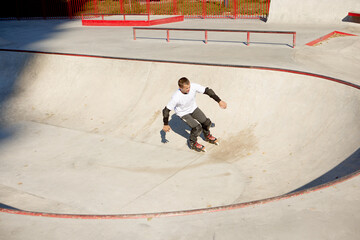 Energetic man on roller skates in motion at modern roller skate park. Roller skater doing dangerous and daring tricks. Sport, health, speed, and energy