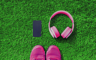 Close up sneakers with pink wireless headphones and blank copy space smartphone screen on grass background, top view