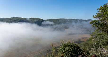 looking down through morning mist in to a valley with agricultural patterned fields, distant hills...