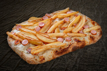 Pizza Patate with viennese sausages, potato fries, mozzarella, cheese sauce, pesto. Roman pizza rectangular on wood background