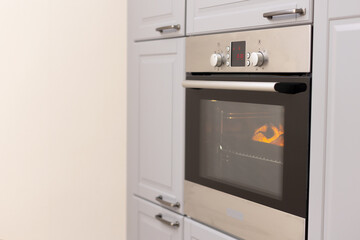 The included oven in the kitchen with gray facades. Slices of orange pumpkin are baked in the oven.