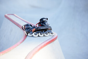 Pair of black inline skates lying on ramp at skate park. Sport equipment, footwear concept