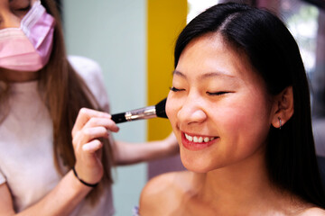 portrait of a smiling young woman receiving a professional makeup in a beauty salon, concept of wellness and body care