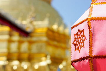 Closeup Thai Lanna style lanterns to hang in front of the golden pagoda at Thai temple under blue sky background.