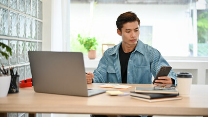Fototapeta na wymiar Smart young Asian businessman or male freelancer using his smartphone