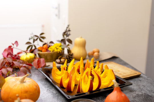 Orange Pumpkin Cut Into Slices And Laid Out On A Baking Sheet. Against The Backdrop Of Beautiful Autumn Leaves And Pumpkins. Cooking In The Kitchen. Food Preparation For Thanksgiving And Halloween.