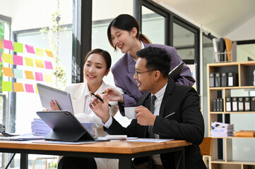 Team of Asian businesspeople brainstorming and checking project details on tablet