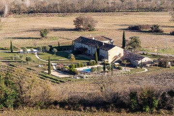 Old traditional French farm made of stone in the middle of a field and surrounded by trees (cypress) in Lussan, Gard, France.