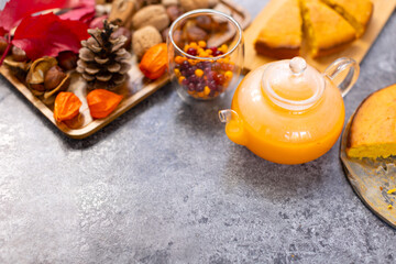 A glass teapot with a beautiful orange pie drink on a gray table. Beautiful background with pumpkin pie and berry tea on the kitchen table with copy space.