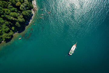 Top view of a sailboat anchored off a rocky coast - obrazy, fototapety, plakaty