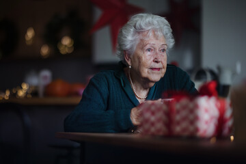 Unhappy senior woman sitting alone and waiting for family during Christmas Eve.Concept of solitude...