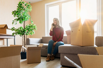 Fototapeta premium A woman is sitting on the couch and talking on the phone in her new apartment. The concept of a happy life in a new place