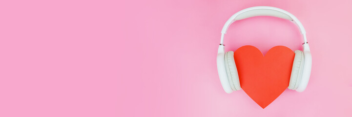 White wireless headphones are put on a red heart on a pink background. The concept of love for...