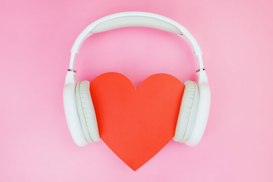 White wireless headphones are put on a red heart on a pink background. The concept of love for music, passion for composing, entertainment.